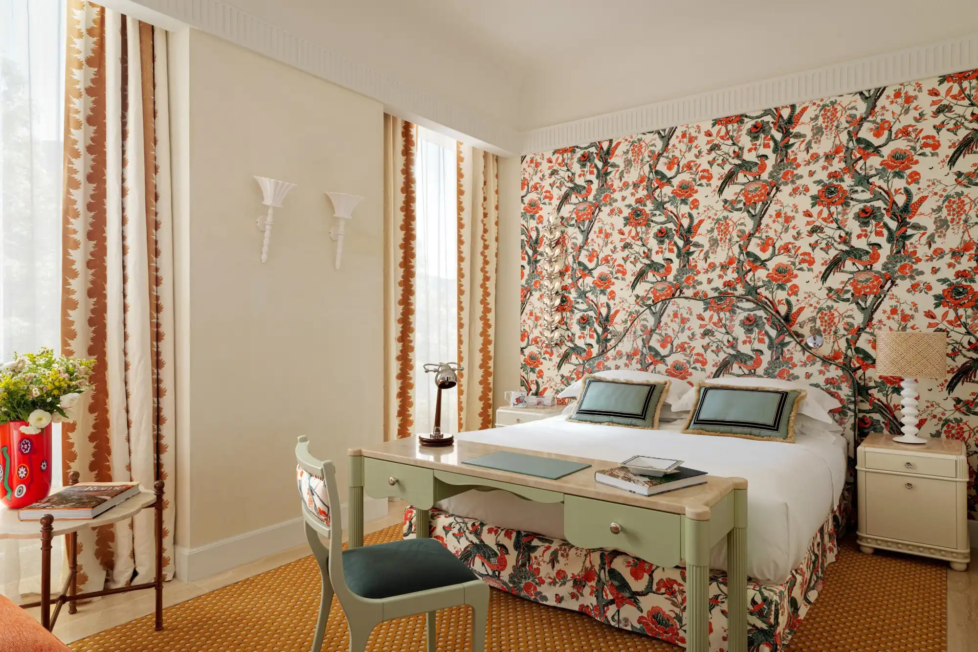 Vibrant hotel room with floral wallpaper, green desk, and artistic design details